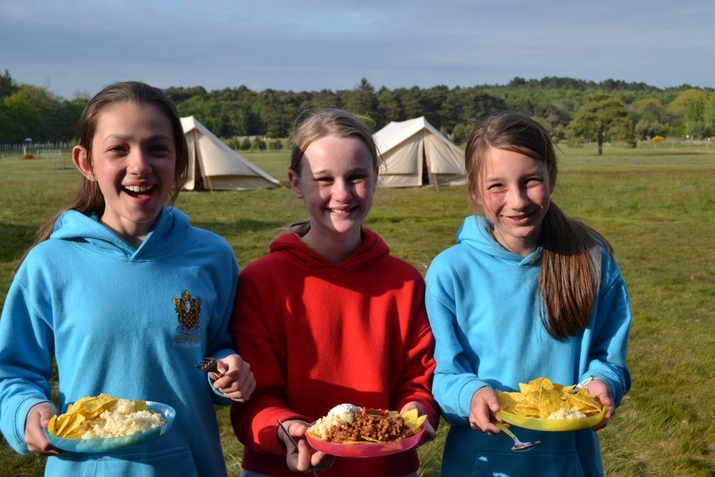 Three girls with three plates of food on the camp site